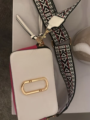Marc Jacobs väska - säljer en Marc Jacobs väska, i färgerna rosa, ljusrosa & vit. Den är inte äkta men ser äkta ut. Väldigt fint skick knappt använd. 300kr