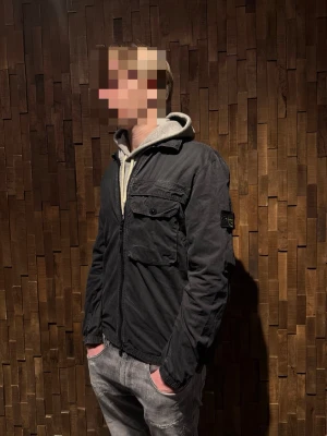 Svart jacka från Stone Island - Säljer en svart jacka från Stone Island med dragkedja framtill. Jackan är äkta  och nypris kostar den runt 8000kr. Jackan är i Vädligt bra skick 8-9/10. Storleken är XL men sitter mer som M-L. Modellen är 186cm och väger 75kg och den sitter bra på han! Priset går att diskutera, hör gärna av er vid intresse eller vid fler frågor! Riktigt snygg tunn jacka nu inför våren!🤩