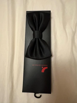 Svart sidenfluga i presentförpackning - Stilren svart fluga i siden från Dressmann, levereras i en elegant presentförpackning. Perfekt accessoar för att lyfta din outfit med en klassisk touch. Flugan har en slät och glansig yta som ger ett exklusivt intryck.