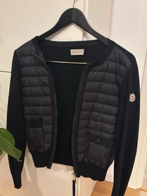  moncler cardigan - Snygg svart cardiganjacka från Moncler med quiltad framsida och två fickor med knappar. Finns qr kod som äktighetsbevis! Enda defekten är att lappen tappat fäste då jag haft den i 3 år, men väldigt omhändertagen 
