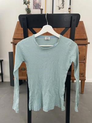 Randig långärmad topp Mads Nørgaard - Långärmad topp från Mads Nørgaard i ljusblått och ljusgult med smala ränder. Modellen är figurnära med rund halsringning och ribbad struktur. Perfekt för en avslappnad och trendig look.