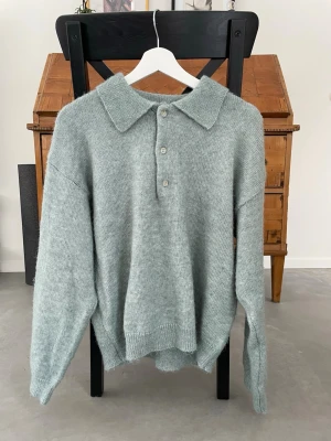 Ljusgrön stickad tröja från Lindex - Mysig ljusgrön stickad tröja från Lindex med stor krage och tre knappar framtill. Tröjan har avslappnad passform, långa ärmar och ribbade muddar. Perfekt för lager på lager och enkel att styla till olika outfits.