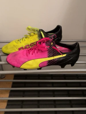 Puma Evospeed - Säljer ett par riktigt snygga fotbollsskor från Puma i färgerna rosa, gul och svart. Skorna har klassisk låg profil, snörning och mönstrad ovandel i syntetmaterial. Perfekta för dig som vill sticka ut på planen med färgstark stil.