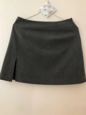 Djerf Avenue kjol - Stilren grå minikjol från Djerf Avenue i klassisk modell. Kjolen har en liten slits framtill som ger en snygg detalj och är tillverkad i ett mjukt och bekvämt material. 