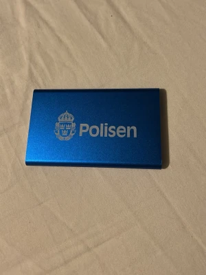 Blå powerbank Polisen USB - Blå powerbank i metall med Polisen-logga. Utrustad med USB-utgång och micro-USB-ingång samt indikatorlampor och strömknapp. Perfekt för att ladda mobilen eller andra enheter på språng.