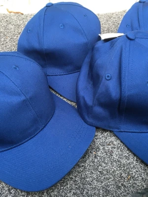 Klassisk blå keps i bomull - Snygg och enkel blå keps med böjd skärm och sex paneler. Kepsen är tillverkad i ett slitstarkt bomullstyg och har ventilationshål upptill. Perfekt för dig som vill ha en stilren och tidlös look. 4 st. Jag samlar på kepsar, så de är sparsamt använda och alla har kvar stuket från när de var nya. När jag skickar en keps så gör jag det med mycket vaddering och alltid i en hård kartong. ( är nog ensam om för begagnade kepsar. 