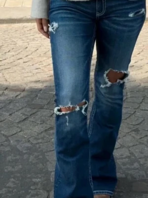 Blå slitna bootcut jeans - Säljer ett par blå bootcut jeans med slitningar och hål på låren och knäna. Jeansen har en klassisk femficksmodell och är tillverkade i denim med en snygg tvätt. Perfekta för en avslappnad och trendig look. Från Gina Young 14+ i storlek xs tror de är tall men inte helt säker o dem är i jättebra skick!!❤️