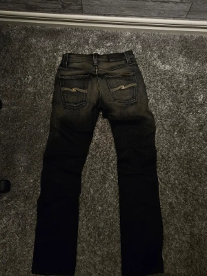 Svarta Nudie Jeans, storlek 29/32 - Hejsan! Säljer nu mina otroligt snygga nudie jeans. Jeansen är svarta med sjukt snygga fades! mått finns nedan🙌 Model:Slim jim(slim bootcut/straight fit) Storlek: 29/32🤟 Skick:10/10❤️‍🔥 Mått: Midja=ca 37cm Längd= ca 103cm  Tveka inte på att höra av dig för fler bilder, mått och frågor☺️  OBS: måtten kan vara fel med 1-2cm, har gjort mitt bästa med att mäta så korrekt som möjligt!🔥