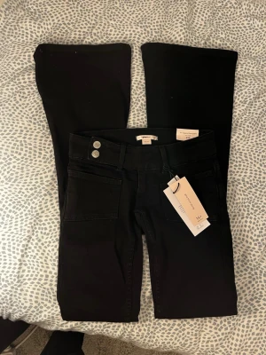 Svarta bootcut-jeans från Gina tricot - Svarta bootcut-jeans i tall från Gina tricot med två knappar i midjan och stora fickor fram. Baksidan har snygga broderade bakfickor med svarta paljettdetaljer. Säljer då de är för små men är helt nya. 😊