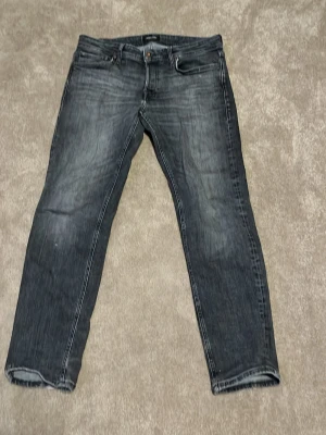 Mörkgrå slim fit jeans - Säljer ett par mörkgrå tapered jeans, modell Mike. Storlek 33/30 och har lagats mellan benen och har lite defekter där men inget som syns och det går att laga. 