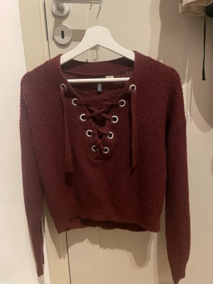 Vinröd stickad tröja med snörning - Vinröd stickad tröja med snygg en snörning framtil. Från hm men säljs inte längre och storlek XS. Inte jätteliten i storlek! 