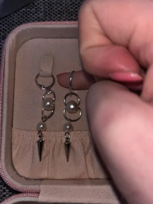 Silvriga örhängen med pärlor och spikes - Säljer ett par unika silvriga örhängen med två ringar, vita pärlor och coola metallspikar längst ner. Örhängena har en modern design med blandning av klassiska pärlor och edgy detaljer. Perfekta för dig som vill sticka ut lite extra.