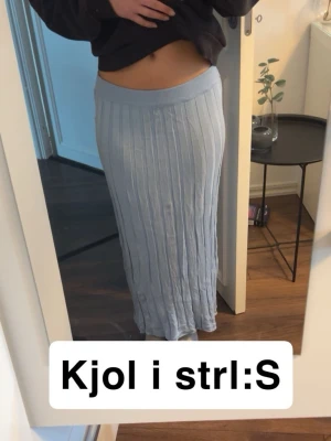 Ljusblå ribbad maxikjol - Säljer en ljusblå maxikjol med ribbad struktur och bred resår i midjan. Kjolen har en rak och lång passform som ger en avslappnad men ändå stilren look. Perfekt att matcha med en croppad tröja eller hoodie. Fint skick förutom skrynklig då den inte används men går att fixa me en tvätt eller strykning