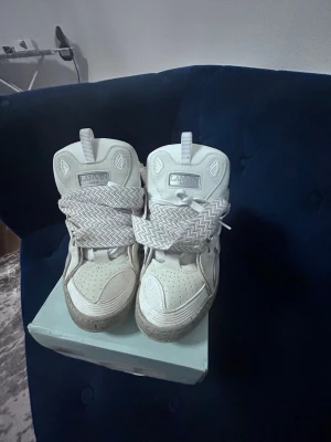 Lanvin vita high top sneakers - Lanvin high top sneakers i vitt läder med breda, mönstrade skosnören i zigzag-stil. Skorna har perforerad tå, tjock sula och detaljer i mesh på sidorna. Klassisk high top-design med robust känsla och modern look.