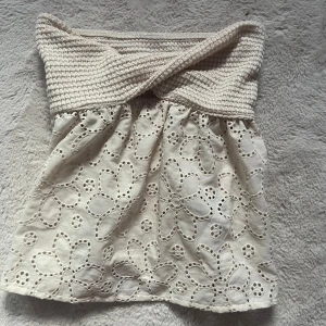 Tube top - Supersöt vit tubtopp med virkad twistad överdel och broderade blommor på nedre delen. Toppen är ärmlös och har en luftig känsla, perfekt för varma dagar. Snyggt mönster och unik detalj med den virkade delen upptill.