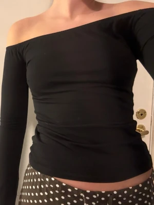 Svart offshoulder topp - Snygg svart offshoulder topp med lång ärm och tight passform. Toppen har en stilren och enkel design som framhäver axlarna. Perfekt att matcha med både jeans och kjol för en trendig look. Använd max 3 gånger