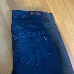 Mörkgrå jeans från Dondup - Säljer ett par mörkgrå/svarta jeans från Dondup med klassisk femficksmodell och smal passform. Jeansen har en diskret D-detalj på bakfickan och röda sömmar vid linningen. Perfekta för en stilren och avslappnad look. Har ett litet hål i framfickan på insidan som lätt går o sy ihop o inte syns vid användning därav priset. 