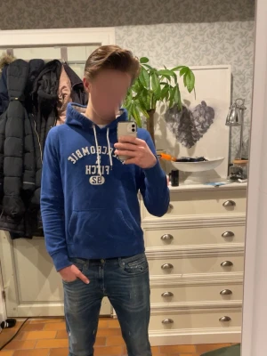 Blå hoodie från Abercrombie & Fitch - Mysig blå hoodie från Abercrombie & Fitch med broderad text på bröstet. Hoodien har vit dragsko, känguruficka. Perfekt för kalla dagar och chill outfits. Passar strl: S, vid frågor eller funderingar skriv gärna!