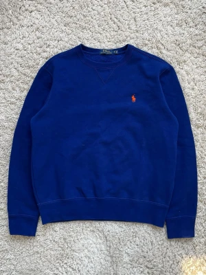 Blå Ralph Lauren sweatshirt i storlek S - Clean Blå Ralph Lauren sweatshirt med orange logga i 84% bomull och 16% polyester  Mycket bra skick, sömmen har släppt lite i nacken men absolut inget som påverkar användningen   Storlek S  Axelbredd: 45 cm Längd: 60 cm