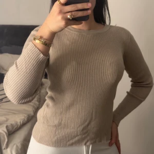 Beige ribbad tröja från Vila  - Säljer en beige ribbad långärmad tröja från Vila. Tröjan har rund halsringning och är figurnära i modellen. Perfekt basplagg i mjukt och stretchigt material som passar till det mesta.