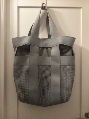 NWT Cos Grå Tote Bag  - NWT Cos Grå Tote Bag   Shopparen, omgjord. Designfokuserad väska med överlagrade remdetaljer och en dämpad finish (innerväskan kan öppnas). 46 x 36 x 18 cm  Titta gärna på mina andra annonser!