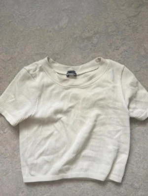 Ribbad croppad vit topp strl S - En enkel och stilren croppad topp i ribbad bomull. Toppen är vit, har korta ärmar och rund halsringning. Perfekt att matcha med höga jeans eller kjol. 