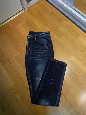 Dsquared2 jeans - Snygga mörkblå jeans i slim fit-modell med slitna detaljer och coola färgstänk. Klassisk femficksdesign och dragkedjegylf. Perfekta för en trendig streetstyle-look.