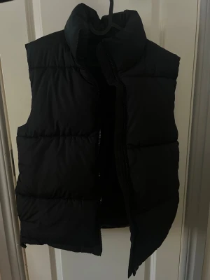Svart puffad dunväst / varm dunväst - Helt oanvänd stilren svart dunväst med hög krage och breda puffade paneler. Enkel och clean design utan synligt märke, passar till det mesta.