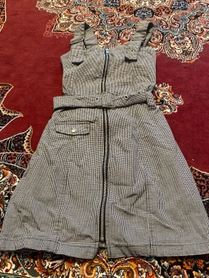 Rutig omlottklänning med bälte - Snygg ärmlös kortklänning i svartvitt rutigt mönster med breda axelband, bälte i midjan och dragkedja framtill. Klänningen har en ficka med knappdetalj och markerad midja för en cool och trendig look.