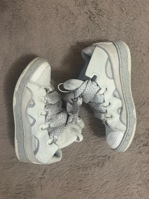 lanvin curb - Unika vita high top sneakers med breda, mönstrade snören i zigzag-stil. Skorna har perforerade detaljer på tån, förstärkta partier och en robust sula. Materialet är en mix av läder och textil. Perfekta för dig som vill sticka ut med din stil.