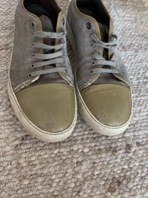 Lanvins - Snygga sneakers i grå mocka med olivgröna detaljer på tån och runt kanten. Skorna har vita sulor och grå skosnören. Perfekta för dig som gillar en stilren men ändå unik look. Passar till det mesta och ger en cool touch till outfiten.