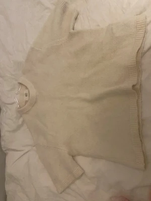Beige tröja & rosa kofta, stickade - Två stickade plagg: en beige tröja med rund hals och ribbade muddar samt en rosa kofta med knappar framtill och ribbad struktur. Båda har kortare ärmar och är perfekta för lager på lager. Snygga basplagg till garderoben.