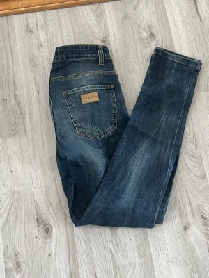 Mörkblå raka jeans Just Jeans - Snygga mörkblå jeans från Just Jeans med raka ben och klassisk femficksdesign. Jeansen har en läderpatch på bakfickan och subtila slitningar för en avslappnad look. Perfekta till vardags och passar till det mesta i garderoben.