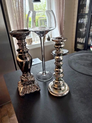 Tre ljusstakar i olika stilar - Säljer tre unika ljusstakar: en hög glasljusstake med bred kupa, en silverfärgad ljusstake med rundad fot och en dekorerad ljusstake i metall med fyrkantig fot. Perfekta som inredningsdetaljer för att skapa mysig stämning hemma.