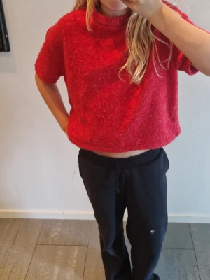 Röd stickad tröja, Gina Tricot - Säljer en röd stickad tröja från Gina Tricot med kort ärm och rund hals. Tröjan har en lite boxig, croppad passform och är gjord i ett mjukt, luddigt material. Perfekt för att ge din outfit en färgklick!