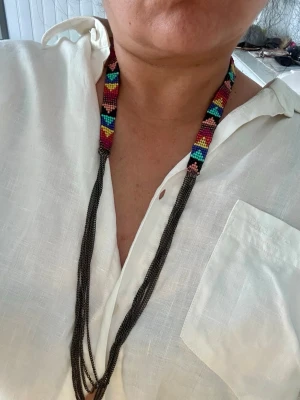 Färgglatt pärlhalsband med kedjor - Unikt halsband med handgjorda pärlor i regnbågens färger och geometriskt mönster. Halsbandet har flera tunna svarta kedjor som hänger ner och ger en cool kontrast till de färgglada pärlorna. Perfekt för dig som vill sticka ut med accessoarer!