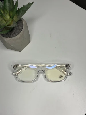 Chrome hearts blue eye glasses - Säljer ett par stilrena solglasögon med transparent båge och rektangulära glas. Glasen är ljusa och bågarna har en modern, kantig design som ger en clean look. Perfekta för dig som vill ha något trendigt och unikt.