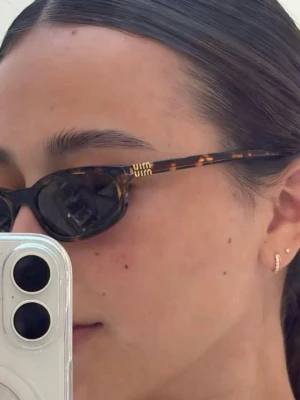Bruna Miu Miu solglasögon - Snygga solglasögon från Miu Miu med brunmelerat, smalt cat eye-båge och mörka glas. Bågarna har en klassisk och trendig look med diskret logga på sidan. Perfekta för att lyfta din stil under soliga dagar.