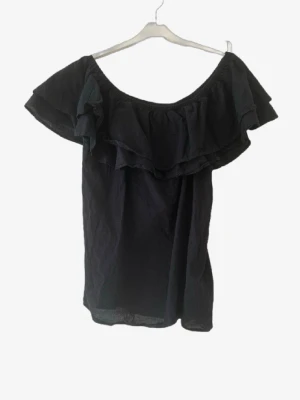 Svart offshoulder topp med volang🌸 - Trendig svart offshoulder topp med bred volang runt axlarna. Perfekt för dig som vill ha en luftig och snygg topp till sommaren. Tillverkad i ett lätt tyg som ger en skön känsla och passar till många olika stilar.