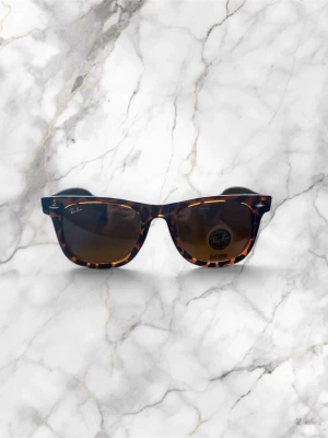 Ray-Ban leopardmönstrade Wayfarer - Ray-Ban Wayfarer solglasögon med leopardmönstrad båge i syntet och bruna glas. Klassisk fyrkantig form och Ray-Ban-logga på sidan ger en ikonisk och trendig look. Perfekt accessoar för soliga dagar.