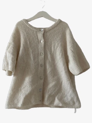 Beige kofta med knappar🌸 - Mysig beige kofta med korta ärmar och knäppning framtill. Koftan har en lös passform och är tillverkad i ett ribbstickat material som ger en avslappnad look. Perfekt att slänga över en t-shirt för extra lager.