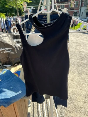 Svart ribbad linnetopp från Gestuz - Snygg svart ribbad linnetopp från Gestuz med unik asymmetrisk halsringning och cut-out detalj vid axeln. Toppen är ärmlös och har en tight passform som ger en trendig look. Perfekt att styla med jeans eller kjol för en cool outfit.