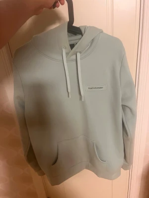 Ljusgrön hoodie från Peak Performance - Snygg ljusgrön hoodie från Peak Performance med broderad logga på bröstet. Klassisk modell med huva och dragsnören samt en stor magficka framtill. Tillverkad i mjukt och bekvämt material, perfekt för en avslappnad stil. Tror det är XL för barn strl 