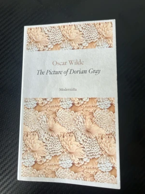 The Picture of Dorian Gray - Oscar Wilde - Snygg pocketbok av Oscar Wilde, 'The Picture of Dorian Gray', utgiven av Modernista. Omslaget har ett elegant blommönster i beige och vitt. Perfekt för dig som gillar klassisk engelsk litteratur och vill ha en stilren bok i bokhyllan.