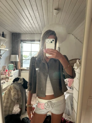 Kort rutmönstrad kavaj - Snygg kort kavaj med rutmönster i grått och svart. Kavajen har trekvartsärmar med knappdetaljer vid ärmsluten och en enkel knäppning framtill. Perfekt för att lyfta vilken outfit som helst med en trendig touch.