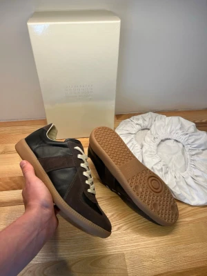 Maison Margiela gats - Riktigt feta Maison margiela gats i färgen brun svart. Jag köpte skorna på vestieire helt nya men säljer nu de eftersom de var för små. Skorna är i storlek 42 men de e lite små på mig som har storlek 42-43, så jag skulle säga att storleken är 41,5-42. Original box och två dustbags följer med som det ska. Skorna är äkta, vilket du kan se på bilderna. Kolla på nån äktehetsverifierings video på YouTube om du vill äktehets checka dem själv. Hör av dig vid minsta fråga eller fundering!