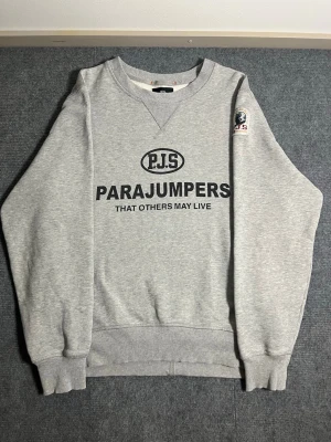 Parajumpers – Grey Sweatshirt (L) - Authentic Parajumpers sweatshirt in classic grey. Size L, length 70 cm, width 58 cm – designed for a comfortable and relaxed fit. The front features the bold Parajumpers logo and the signature motto “That Others May Live”, with the recognizable patch on the sleeve adding a premium touch.  ✅ Condition: Excellent – no stains, no damage 💯 Authenticity: 100% genuine, can be verified easily on certilogo.com 🧵 Material: Thick and warm cotton blend – soft, durable, and perfect for cooler days