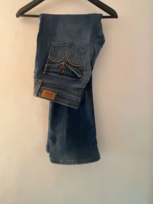 Blå bootcut jeans från Levi's - Säljer ett par klassiska blå Levi's jeans med bootcut passform och snygga kontrastsömmar. Jeansen har fem fickor, knappgylf och en ikonisk läderpatch bak. Perfekta till vardagslooken och passar till det mesta i garderoben.