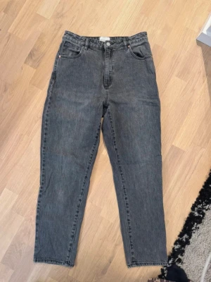 Grå mom jeans från Abrand - Säljer ett par grå mom jeans från Weekday med hög midja och raka ben. Jeansen har klassisk femficksdesign och en liten svart logga på bakfickan. Storlek: W:30 