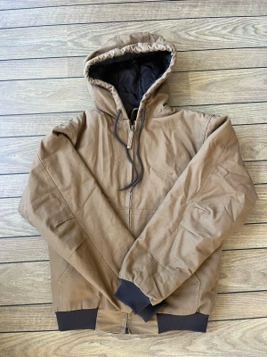 Brun bomberjacka med huva - Väldigt lik den legendariska carhartt WIP active jacket!! Brun bomberjacka med huva och snörning, dragkedja framtill och ribbade muddar. Jackan har två sidofickor och är tillverkad i slitstarkt material. Perfekt som vinterjacka.